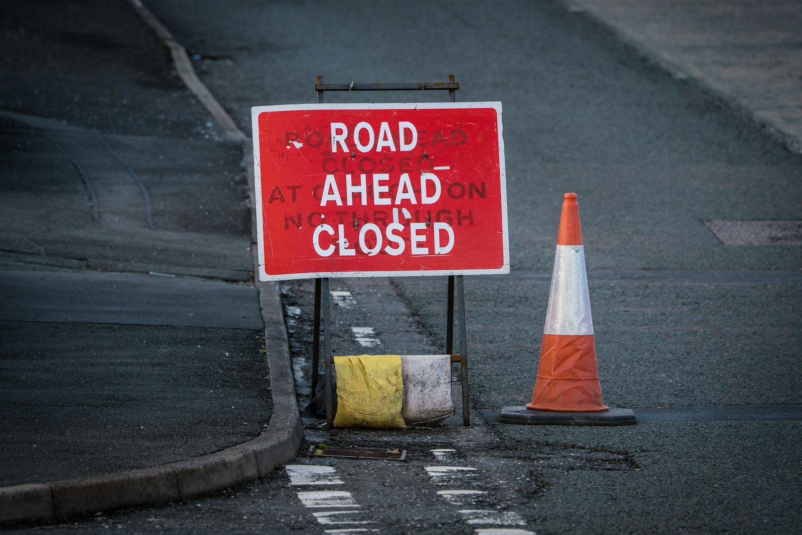 a road closed sign next to a traffic cone